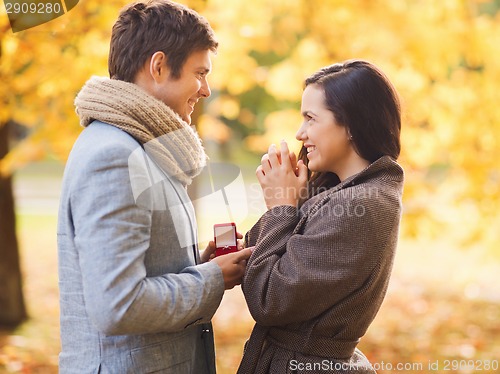 Image of smiling couple with red gift box in autumn park