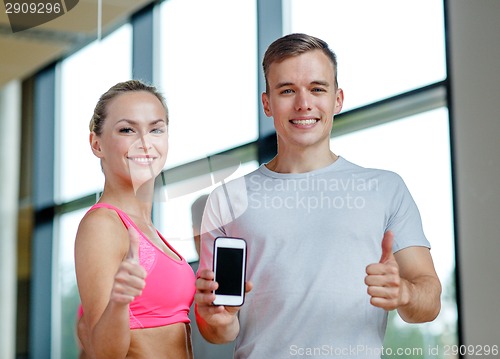 Image of smiling young woman with personal trainer in gym