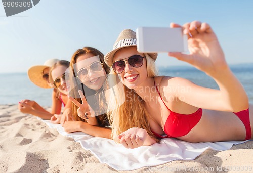 Image of group of smiling women with smartphone on beach