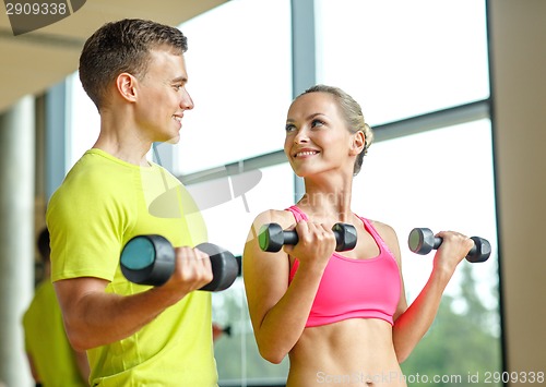 Image of smiling man and woman with dumbbells in gym