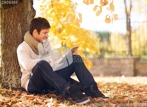 Image of smiling young man with tablet pc in autumn park