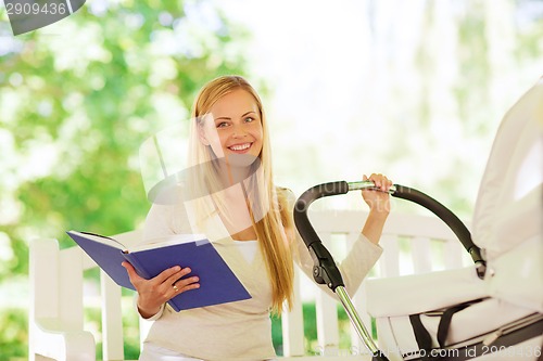 Image of happy mother with book and stroller in park