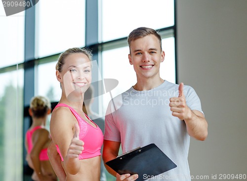 Image of smiling young woman with personal trainer in gym