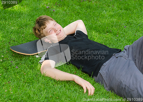 Image of Laughing guy relax on skateboard in park grass