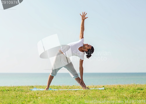 Image of smiling man making yoga exercises outdoors