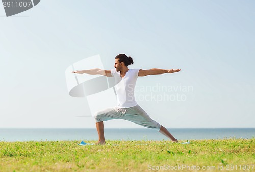 Image of smiling man making yoga exercises outdoors