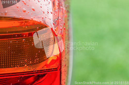 Image of Wet tail lights of modern car against green grass