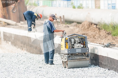 Image of Worker stamps filling brick by road roller