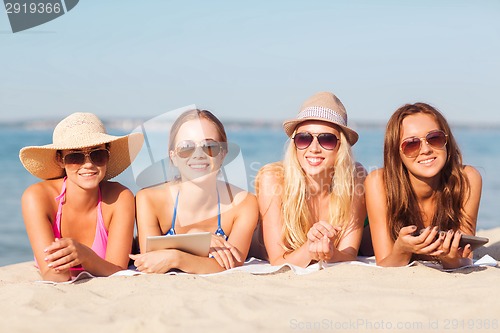 Image of group of smiling young women with tablets on beach