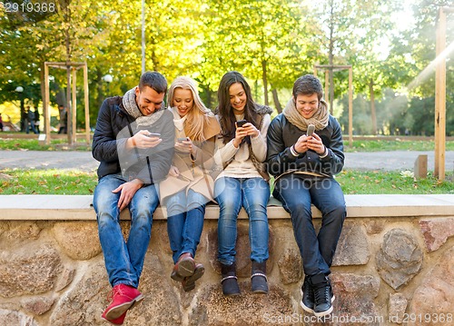 Image of smiling friends with smartphones in city park