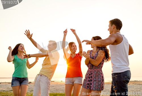 Image of smiling friends dancing on summer beach