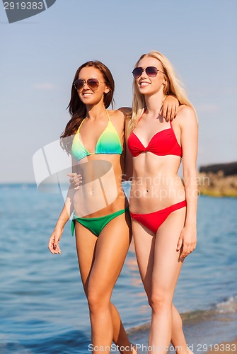 Image of two smiling young women walking on beach