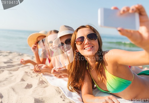 Image of group of smiling women with smartphone on beach