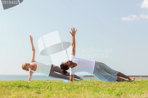 Image of smiling couple making yoga exercises outdoors