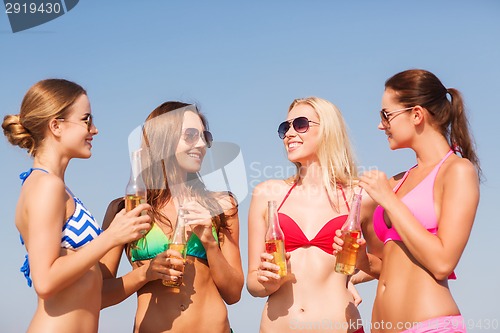 Image of group of smiling young women drinking on beach