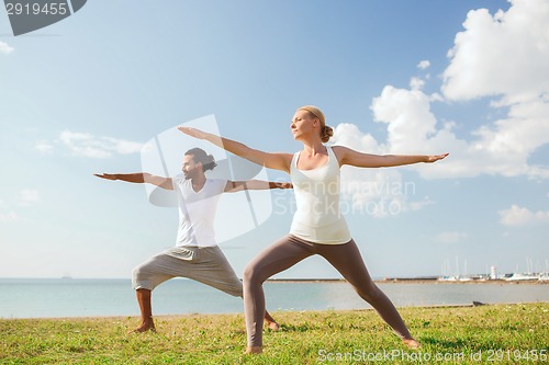 Image of smiling couple making yoga exercises outdoors