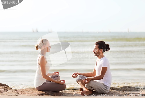 Image of smiling couple making yoga exercises outdoors