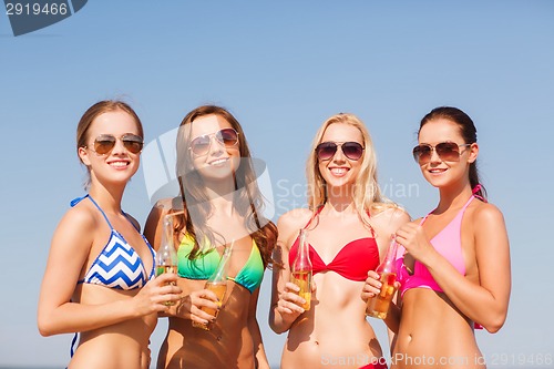 Image of group of smiling young women drinking on beach