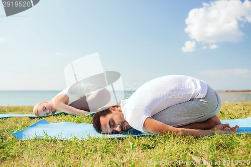 Image of smiling couple making yoga exercises outdoors