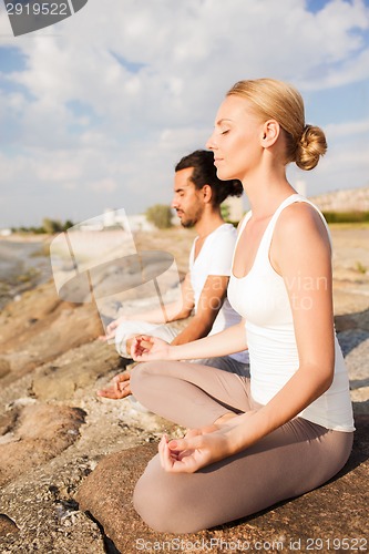 Image of smiling couple making yoga exercises outdoors