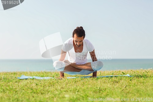 Image of smiling man making yoga exercises outdoors