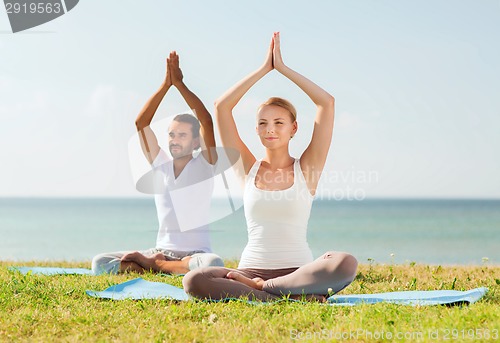 Image of smiling couple making yoga exercises outdoors