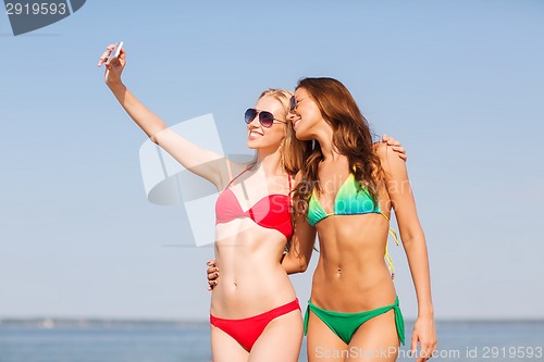Image of two smiling women making selfie on beach