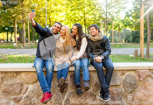 Image of smiling friends with smartphones in city park