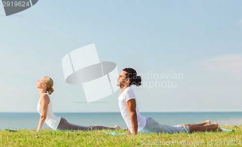 Image of smiling couple making yoga exercises outdoors