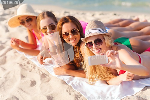 Image of group of smiling women with smartphone on beach