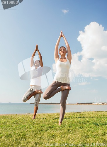 Image of smiling couple making yoga exercises outdoors