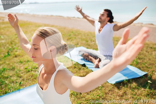 Image of smiling couple making yoga exercises outdoors