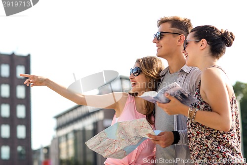 Image of smiling friends with map and city guide outdoors