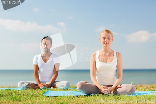 Image of smiling couple making yoga exercises outdoors