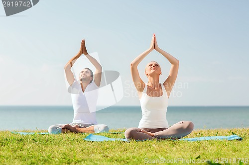 Image of smiling couple making yoga exercises outdoors