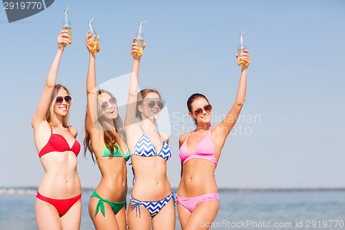 Image of group of smiling young women drinking on beach