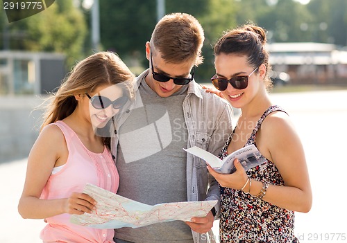 Image of smiling friends with map and city guide outdoors