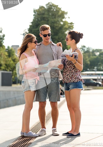 Image of smiling friends with map and city guide outdoors