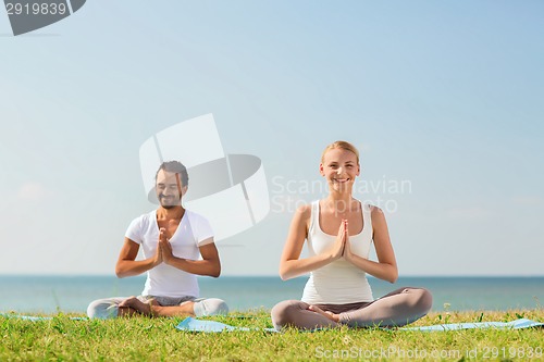 Image of smiling couple making yoga exercises outdoors