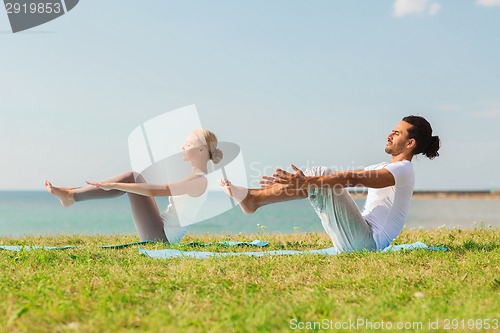 Image of smiling couple making yoga exercises outdoors