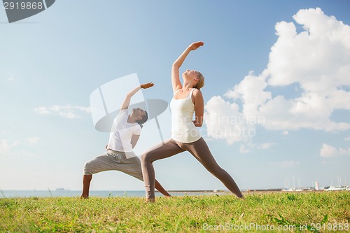 Image of smiling couple making yoga exercises outdoors