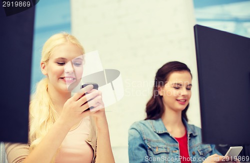 Image of two teens with smartphones in computer class