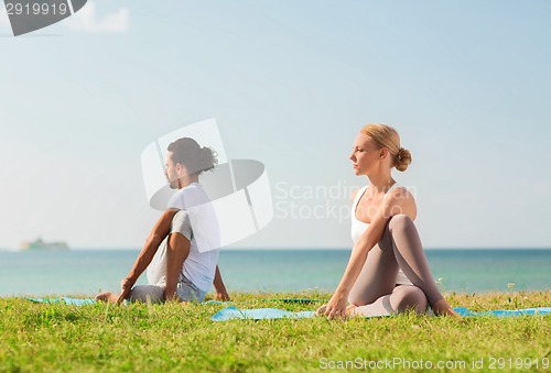Image of smiling couple making yoga exercises outdoors