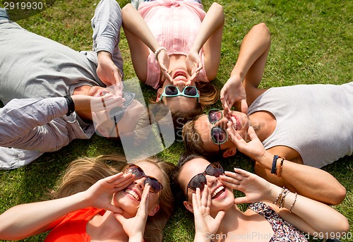 Image of group of smiling friends lying on grass outdoors