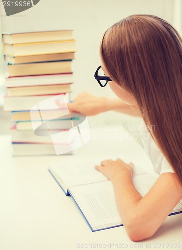 Image of little student girl in eyeglasses with many books