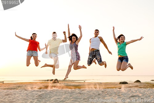 Image of smiling friends dancing and jumping on beach