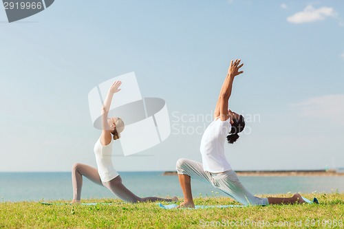 Image of smiling couple making yoga exercises outdoors