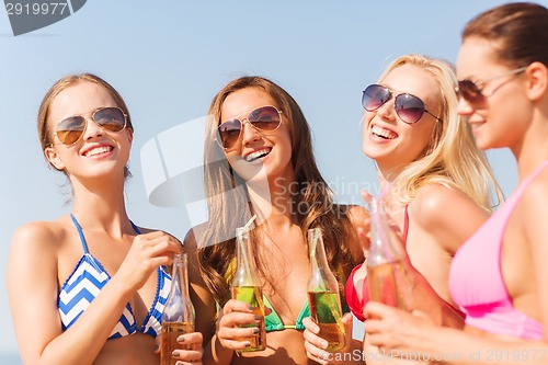 Image of group of smiling young women drinking on beach