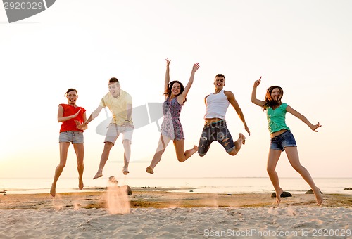Image of smiling friends dancing and jumping on beach