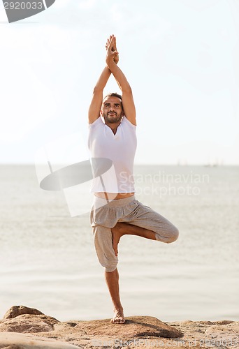 Image of smiling man making yoga exercises outdoors